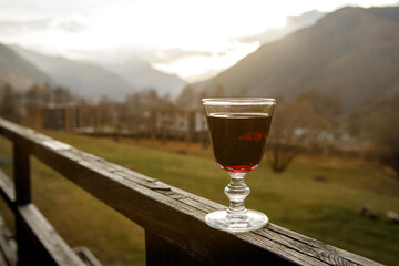 A glass of red liquor against the backdrop of a mountain valley.