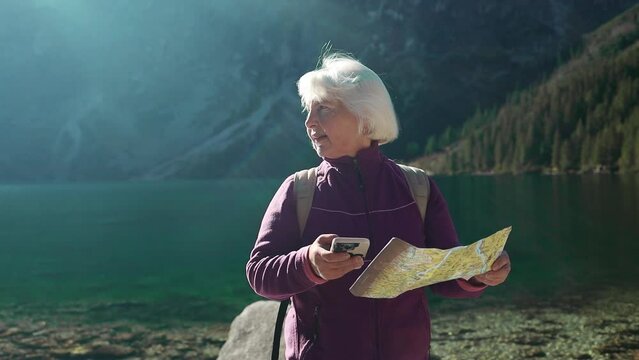 Woman traveler explorer with backpack hiking to the top of the mountain. Tourist hiker senior woman backpacker in mountain read the map. Summer trip in nature. High quality FullHD footage