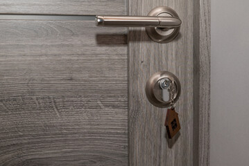 Buy Or Rent concept. Keys with trinket in shape of house in the door keyhole.