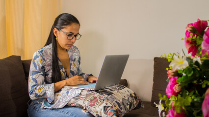 mujer joven latina usando su laptop para trabajar desde la comodidad de su casa 