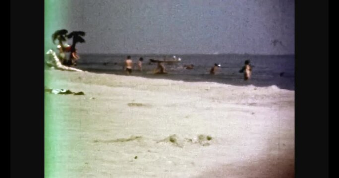 Tropical sandy sea beach with sunbathing people on sunny day. Vacationers swim in blue ocean, white sand. Sea holiday in summer. Beach resort. Vintage color film. Holiday travel archive. Retro 1980s