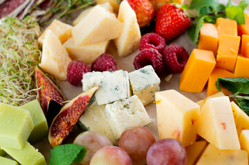 Blurred image of pieces of different cheeses, raspberries, grapes, figs, strawberries and mint. Light snack concept.
