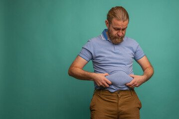 A man with a sad face feels his fat belly on blue background, closeup. Space for text