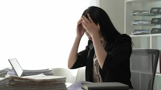 Tired Asian businesswoman reviews documents on table with broken financial data sheets, 4K