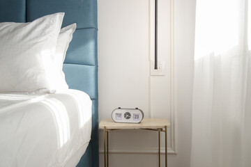Blue king size bed with crisp white bedding and digital alarm clock on the nightstand under beautiful morning sunlights	 - obrazy, fototapety, plakaty