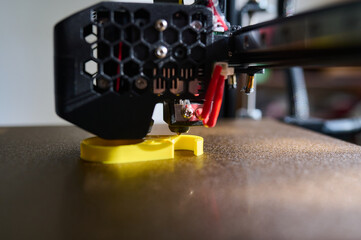 3D printer printing a part made of yellow plastic, close-up view