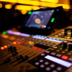 Poster Modern sound mixer console with colorful buttons and sliders, set against the backdrop of a live music venue © 9parusnikov