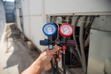Air conditioning, HVAC service technician using gauges to check refrigerant and add refrigerant.	