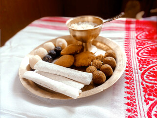 Assamese traditional food items like pitha, laddu, doi sira with assamese gamosa background with japi motifs