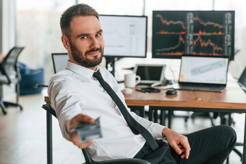 Giving lot of money. Holding in hand. Businessman is sitting by computer and working in the office