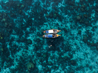 View from above, stunning aerial view of two long tail boats floating on a turquoise water while some tourists snorkel.  Phuket, Thailand.