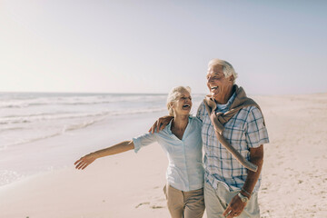 Happy senior couple walking on sunny beach