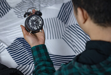 Time management concept. Asian man looking at Black retro alarm clock. Time to wake up for the...
