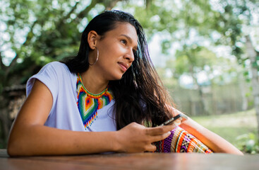 mujer joven de cabello largo  mirando al frente mientras sostiene su telefono movil 