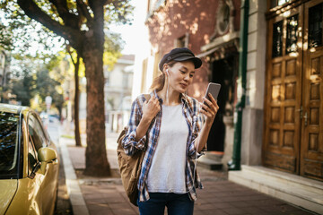 Young woman with headphones using smartphone on city street - Powered by Adobe
