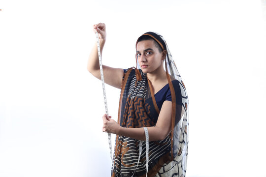 Portrait of a self dependent bald Rural Indian widow holding a measuring tape and working as a tailor in a village in India. She is a bald widow lady wearing a saree.