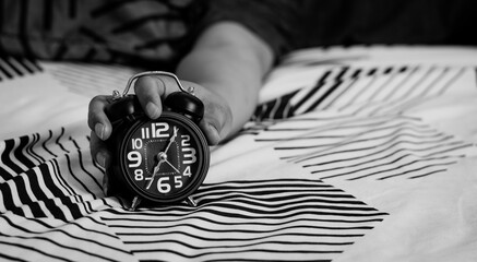 Deadline and Time management concept. Man hands holding Black alarm clock on bed. time to wake up...