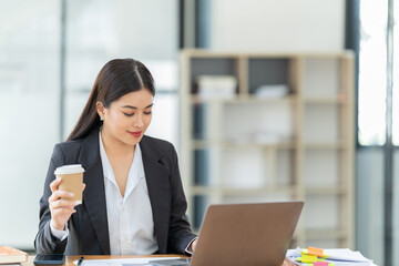 Sharing good business news. Attractive young businesswoman talking on the mobile phone and smiling while sitting at her working place in office and looking at laptop PC.