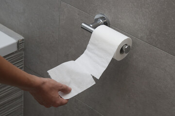 Close up of hand holding toilet paper roll in holder