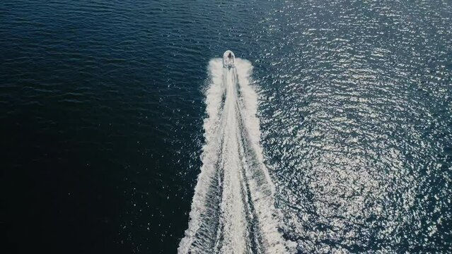 Drone shot of a motorboat cruising at speed over the blue sparkling ocean 