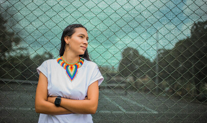 mujer latina en el parque usando ropa comoda y un collar colorida con sus manos cruzadas  - obrazy, fototapety, plakaty