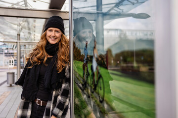 Woman in her mid-thirties with long red hair wearing a cap and black clothing in an urban location.