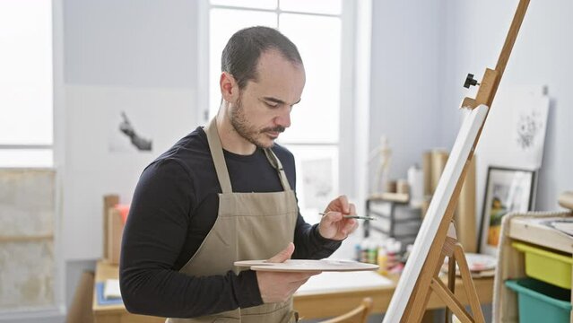 A bald man with a beard paints on a canvas in a well-lit studio, showcasing his creative process and artistic environment.