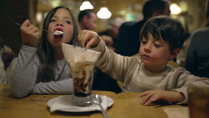 Children Enjoying Ice Cream Sundae Together - Siblings Sharing Dessert at Family Diner During Evening