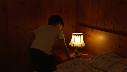 Child turns on bedside lamp inside traditional wooden chalet interior. One little boy turning ON...