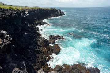 Obraz premium beach landscape with the sea and waves and cliffs of the coasts of the Galapagos Islands in the Pacific Ocean with blue and green water and volcanic rocks