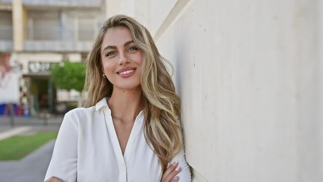 Laughing out loud, vivacious young blonde woman, confidently standing with her arms crossed in an urban street, radiating healthy joy and a contagious smile.