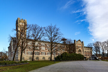 Fototapeta na wymiar Empty esplanade with old main building of former Waterschei mine in background against blue sky, bare trees, Thor Park - Hoge Kempen National Park, sunny autumn day in Genk, Belgium