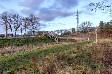 Wooden stairs over a stream on hill in countryside, bare trees and electricity poles against cloudy...