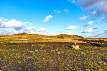 Landscape of open valley plain with sparse yellowish green grass, mountains against blue sky with...