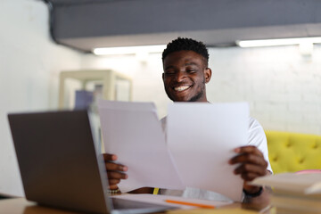 Happy businessman working on a laptop in a modern office or home setting, managing paperwork and exuding professionalism.