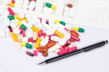 pen, colorful pills and tablets in white background