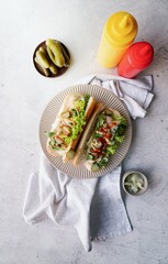 Hot dog with sausage, letuce, cucumber and onion on beige plate on concrete background