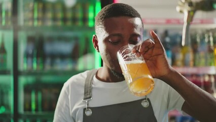 Servant drinks beer at pub counter closeup. African American bartender tastes frothy alcoholic drink resting after hard work in bar. Craft brewery product - Powered by Adobe