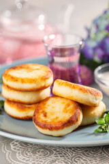 Fried cottage cheese pancakes syrniki served with sour cream and flower tea on a blue dish.