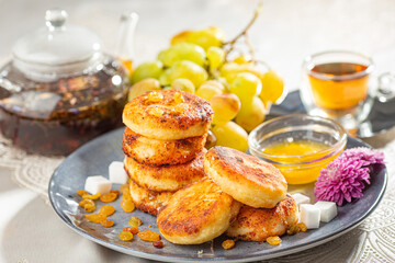 Fried cottage cheese pancakes syrniki with raisins, grapes and honey on a blue dish served with...