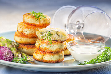 Fried cottage cheese pancakes syrniki with dill and asparagus on a blue plate served with sour cream and wine.