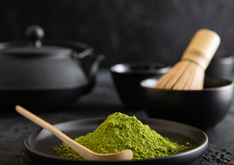Plate with green matcha tea with bamboo spoon and whisk and japanese iron cast kettle on black background.
