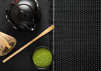 Green matcha tea with bamboo spoon and whis and japanese iron cast kettle on black background.Top...