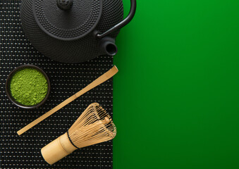 Organic matcha green tea powder with bamboo whisk and spoon and japanese traditional iron cast kettle on green background.Top view.