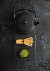 Green matcha tea powder with whisk and iron kettle on stone board on black background.Top view.