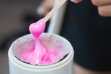 depilation and beauty, sugar paste or wax for hair removal. Preparation of pink wax for sugaring. Close-up of sugar paste or wax honey for hair removal using a wooden wax spatula - obrazy, fototapety, plakaty