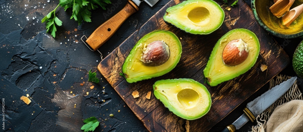 Poster avocado cut in half on a cutting board next to a knife a lemon and two spoons. copy space image. pla