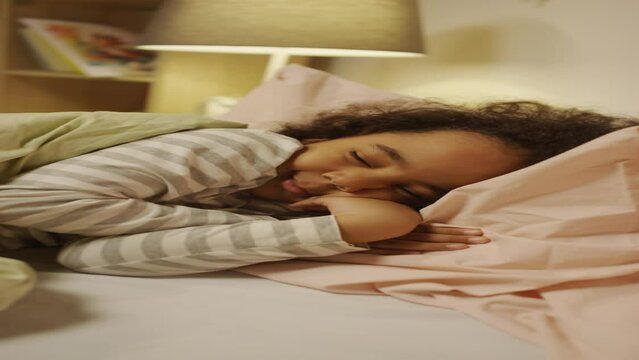 Vertical footage of African American boy smiling while sleeping and sucking thumb in bed at nightVertical footage of African American boy smiling while sleeping and sucking thumb in bed at nightVertic