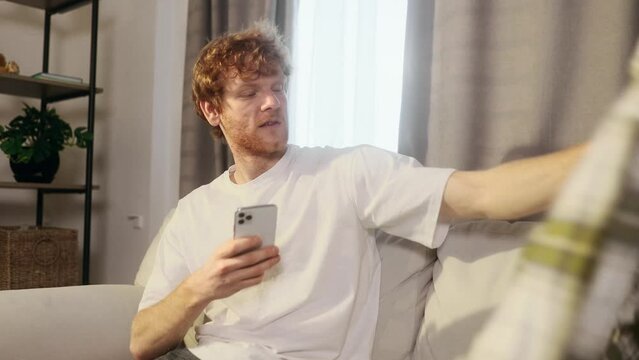 Handsome smiling red haired man taking picture of used clothes shirt on smartphones for post to sell online on internet market charity or recycle at home Second hand clothes concept