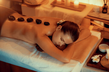 Hot stone massage at spa salon in luxury resort with warm candle light, blissful woman customer...